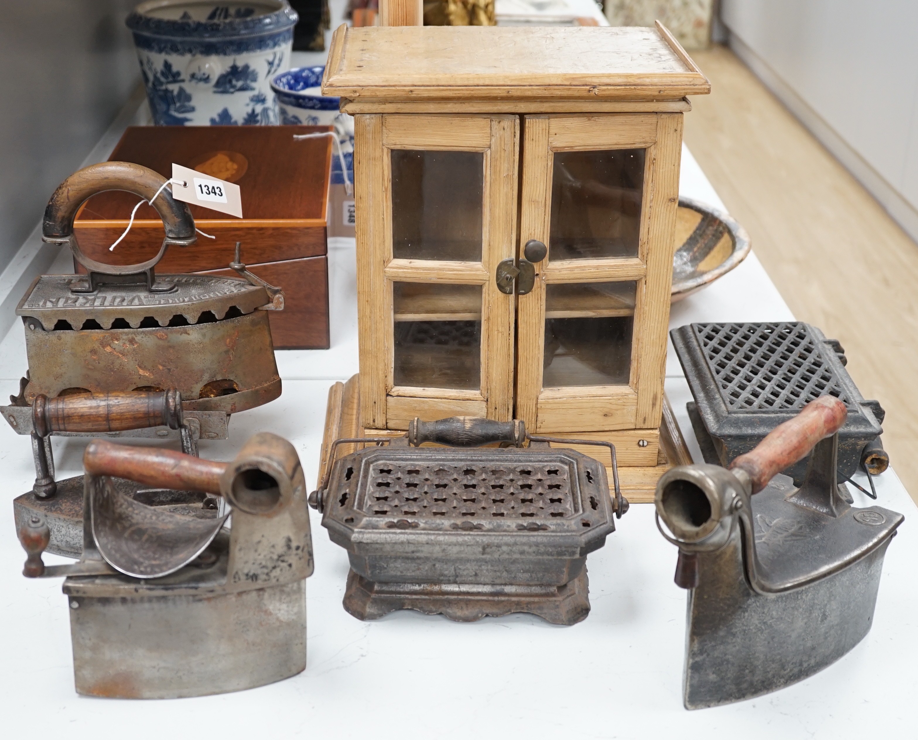 Four French coal/slug irons, three trivets and a stripped pine glazed cabinet, 37cm high